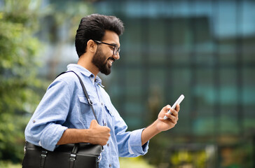 Wall Mural - Happy young eastern handsome man holding smartphone walking outdoor