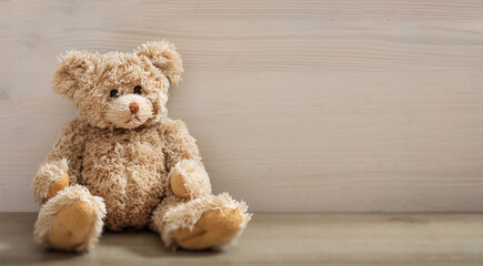 Wall Mural - Teddy bear is sitting on an empty wooden background. Brown lonely sad fluffy animal toy. Copy space