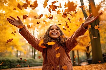 Wall Mural - a little girl throwing autumn leaves in the air with her eyes wide open, smiling and looking up into the camera