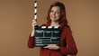 © kinomaster - Medium isolated shot satisfied, happy and relaxed young woman holding an opened movie clicker, slate, clapperboard in front of herself.