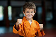 Junge in orangefarbenen Kampfsportanzug trainiert lächelnd in der Kampfsportschule für Kinder, sportliche Entwicklung beim Kampfsportunterricht, erlernen von Koordination und Selbstvertrauen