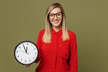 Wall Mural - Young smiling happy fun cheerful woman she wearing red shirt casual clothes glasses holding in hands clock looking camera isolated on plain pastel green background studio portrait. Lifestyle concept.