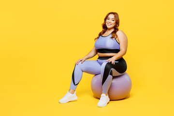 Wall Mural - Full body smiling happy young chubby plus size big fat fit woman wear blue top warm up training sit on fit ball look camera isolated on plain yellow background studio home gym. Workout sport concept.