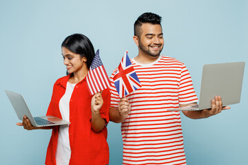 Wall Mural - Young couple two friends family Indian IT man woman wear red casual clothes t-shirt together hold British flag use work on laptop pc computer isolated on pastel plain light blue cyan color background