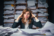Woman sitting at desk covered in papers. This image can be used to represent busy work environment or person dealing with paperwork.