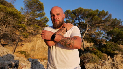 Striking portrait of a man with blue eyes and a beard, set against the picturesque landscape of Cap d'Antibes, France. His tattoos tell a story, embodying a blend of rugged charm and natural beauty