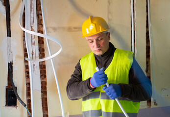 Wall Mural - Caucasian electrician in vest and helmet standing with cable duct in hands during repair works in apartment.