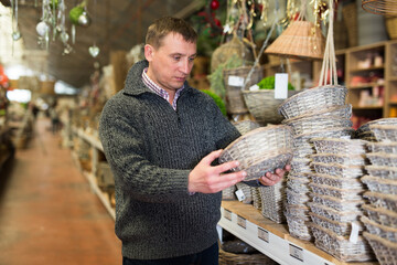 Wall Mural - Puzzled man choosing handmade wickerwork for interior in home decor shop..