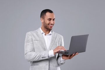 Wall Mural - Young businessman using laptop on grey background