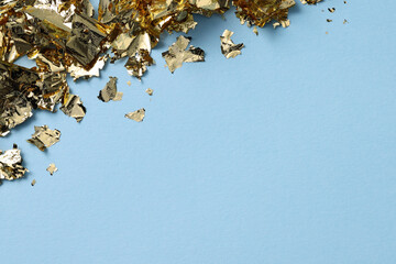 Wall Mural - Many pieces of edible gold leaf on light blue background, top view. Space for text