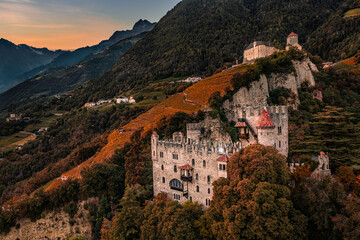 Wall Mural - Merano, Italy - Aerial view of the famous Castle Brunnenburg with Tyrol Castle at background in the Italian Dolomites and colorful sunset sky at autumn afternoon
