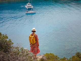 Wall Mural - Asian woman in hat look on views of azure Bay in Mediterranean sea. Travel and vacation concept. Anthony Quinn bay with crystal clear water in Rhodes island, Greece. The most beautiful beach.