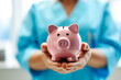 Female doctor or nurse in blue uniform holding pink piggy bank in clinic close up. Life and health insurance, cost of treatment, healthcare