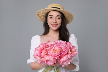 Poster - Beautiful young woman in straw hat with bouquet of pink peonies against grey background