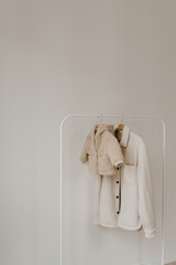 Wall Mural - Autumn outerwear on hanger over white wall. Warm baby's and adult jackets. Aesthetic wardrobe with clothes in neutral colours