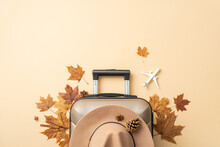 Planning An Autumn Getaway? Behold A Top View Image Of A Gray Suitcase With Autumn Leaves Around And A Charming Felt Hat On A Soothing Beige Background, Perfect For Your Advertisement Or Text
