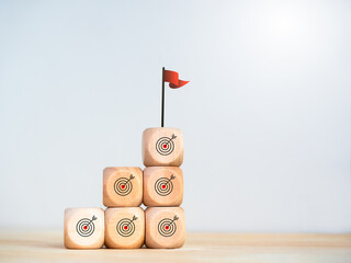 Poster - Business growth, goal plan, success, and economic development concepts. Victory flag on the top on wooden cube blocks as a business graph steps with target dart symbol on table and white background.