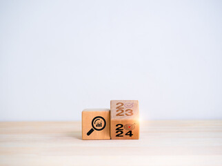 Poster - 2024 new year trend concept. Flipping the 2023 to 2024 year numbers calendar and magnifying glass with graph, trends searching icon on wooden cube blocks isolated on white background with copy space.