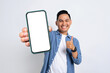 Happy young Asian man in casual shirt showing smartphone with blank screen and thumb up isolated on white background