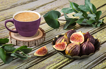 Fresh ripe figs on vintage plate, purple cup of coffee, sprig of eucalyptus, vintage scissors as decor on wooden background.