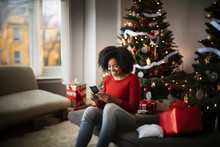 Young African American Woman Ordering Gift During Christmas Holiday At Home Using Smartphone And Credit Card. Shopping Online During Holidays, Internet Banking, Store Online.
