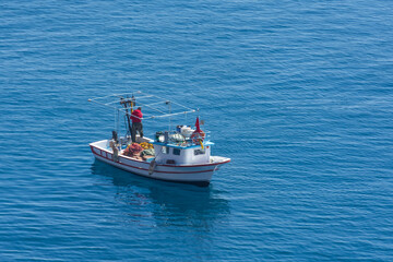 Wall Mural - Small fishing boat with nets follows the sea surface of the Mediterranean Sea view from above aerial away distance.