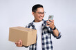 Happy young Asian man in casual shirt holding package box and using mobile phone for online shopping isolated on white background
