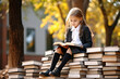 © Keitma - Schoolgirl sitting on a pile of books outdoor , wearing school uniform , kid learning or reading concept