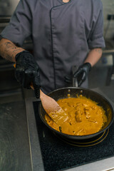close-up of a chef in a professional restaurant kitchen adding sauce to a curry pan stirring the dish