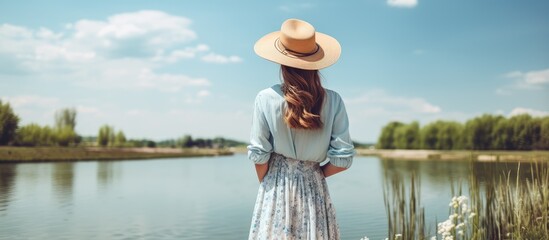 A fashionable lady in summer attire and straw hat poses at a river pier with a beautiful background