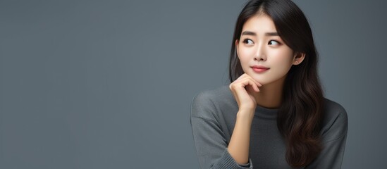 Poster - A woman from Asia looking cute ponders on a gray backdrop