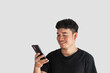 © Apirak - A young man wearing a black t-shirt is happily playing with a mobile phone on a gray background. online social concept. Clipping Path