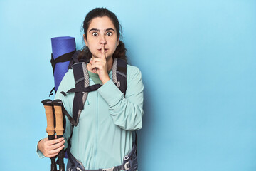 Hiker with backpack and poles on blue keeping a secret or asking for silence.