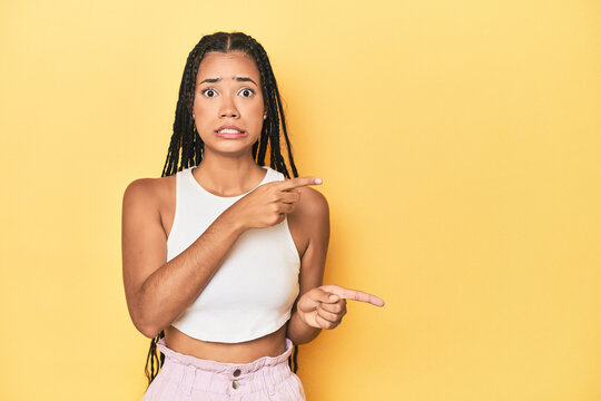 Young Indonesian woman on yellow studio backdrop shocked pointing with index fingers to a copy space.