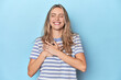 © Asier - Blonde young caucasian woman in blue studio laughing keeping hands on heart, concept of happiness.