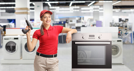 Poster - Repairwoman with a drill standing next to an oven