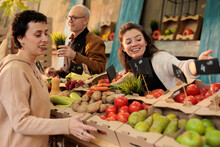 Positive Market Stand Owner Showing Organic Produce To Woman, Presenting Colorful Bio Fruits And Vegetables. Young Farmer Selling Homegrown Eco Products From Personal Local Farm.