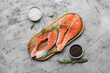 Wooden board with raw salmon steaks and different spices on blue background