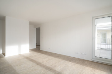 Wall Mural - Unfurnished living room in new apartment. Sunlight enters the room and hits the wooden floor. Walls are white and have electrical outlets,controls and other connections. There is also balcony door.