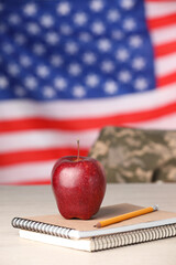 Wall Mural - Notebooks, apple and pencil on light table against flag of USA. Military education