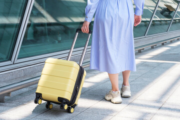 Young woman rolls yellow suitcase near the airport, back view.