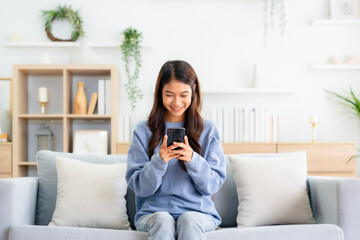 Happy young asian woman relax on comfortable couch at home texting messaging on smartphone, smiling girl use cellphone, chatting online message, shopping online from home