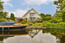 A Boat On The Water In Front Of A House With A Blue Sky And White Clouds Above It, As Seen From Across The