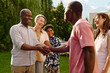 © AnnaStills - Two happy African American men shaking hands while standing in front of camera against their wives and cute boy and greeting one another