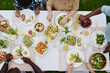 © AnnaStills - Above view of large intercultural family sitting be served table and eating appetizing homemade food while African American man pouring juice