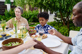 Fototapeta Londyn - Cute little boy holding by hands of his grandparents during pray by table served with homemade food and drinks by outdoor family dinner