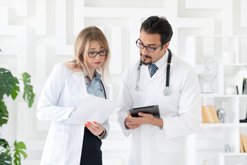 Portrait of two young doctors in white medical gown working in the office of clinic. Colleagues meeting, discussion and health care concept