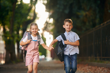 Front view, walking together. Young school children of boy and girl are outdoors