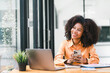 Cheerful young African American pretty woman, entrepreneur in casual wear, smiling, using smartphone and working in a modern office.