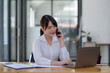 © amnaj - Asian businesswoman modern professional talking with client on the phone with a confident demeanor and effective communication skill. business, marketing, sale and communication project.